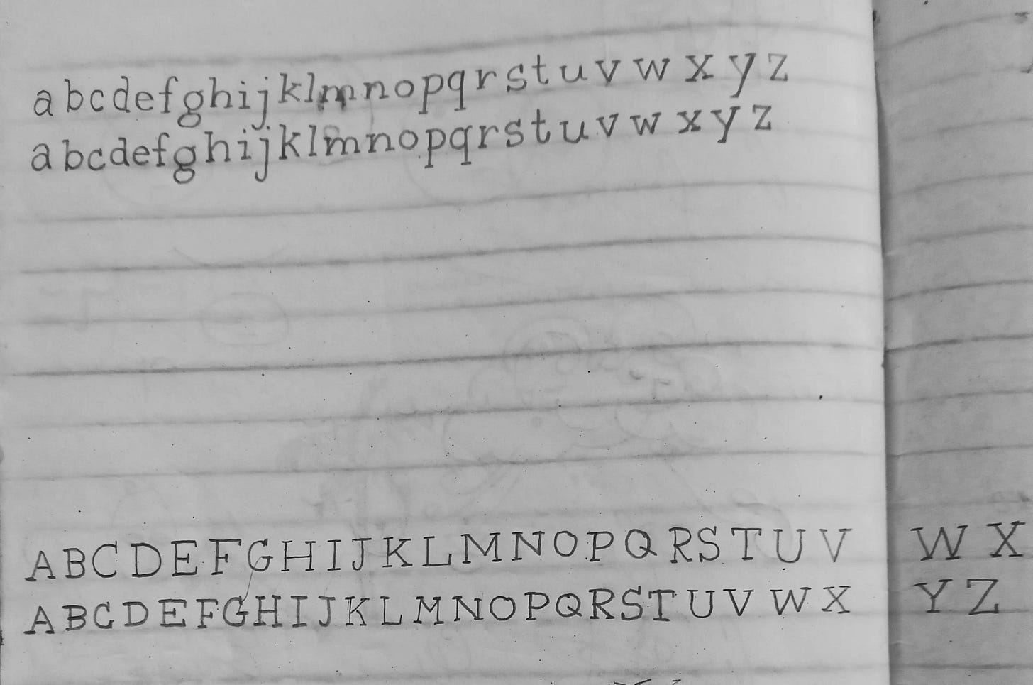 A notebook page showing the typewriter-inspired lowercase and uppercase alphabet written in pencil on lined paper.