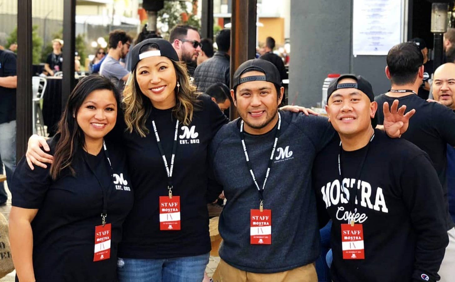 Founders of Mostra Coffee arm in arm at the forefront of the image. An outdoor party in front of a brewery is the background. From left Bev, Jelynn, Sam and Mike.