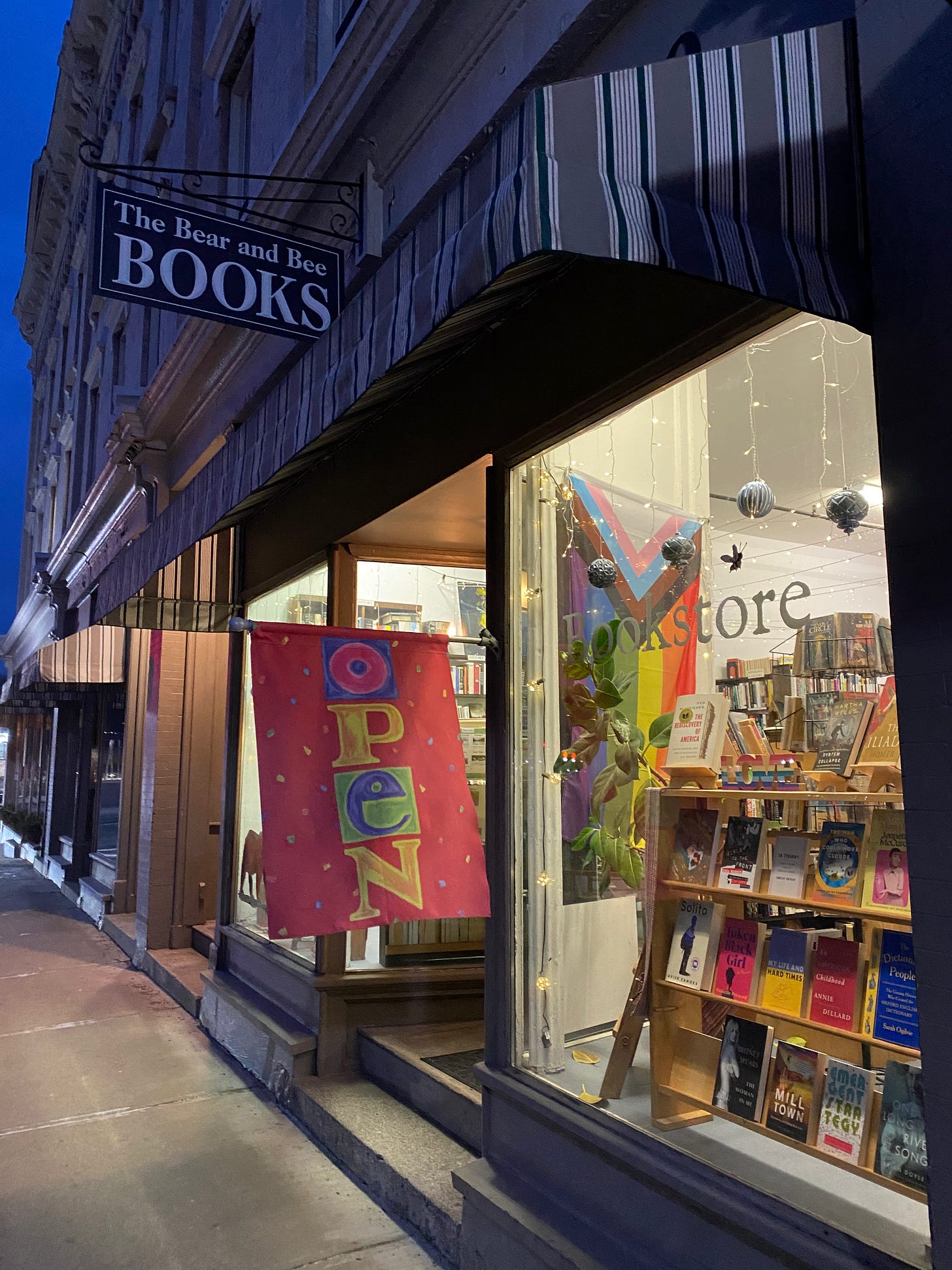 A brightly lit bookshop with a large pride flag hanging in the window.