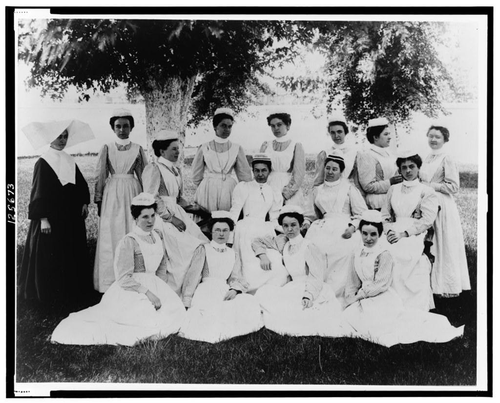 Portrait photograph of a nun and nurses posed sitting and standing under a tree. 