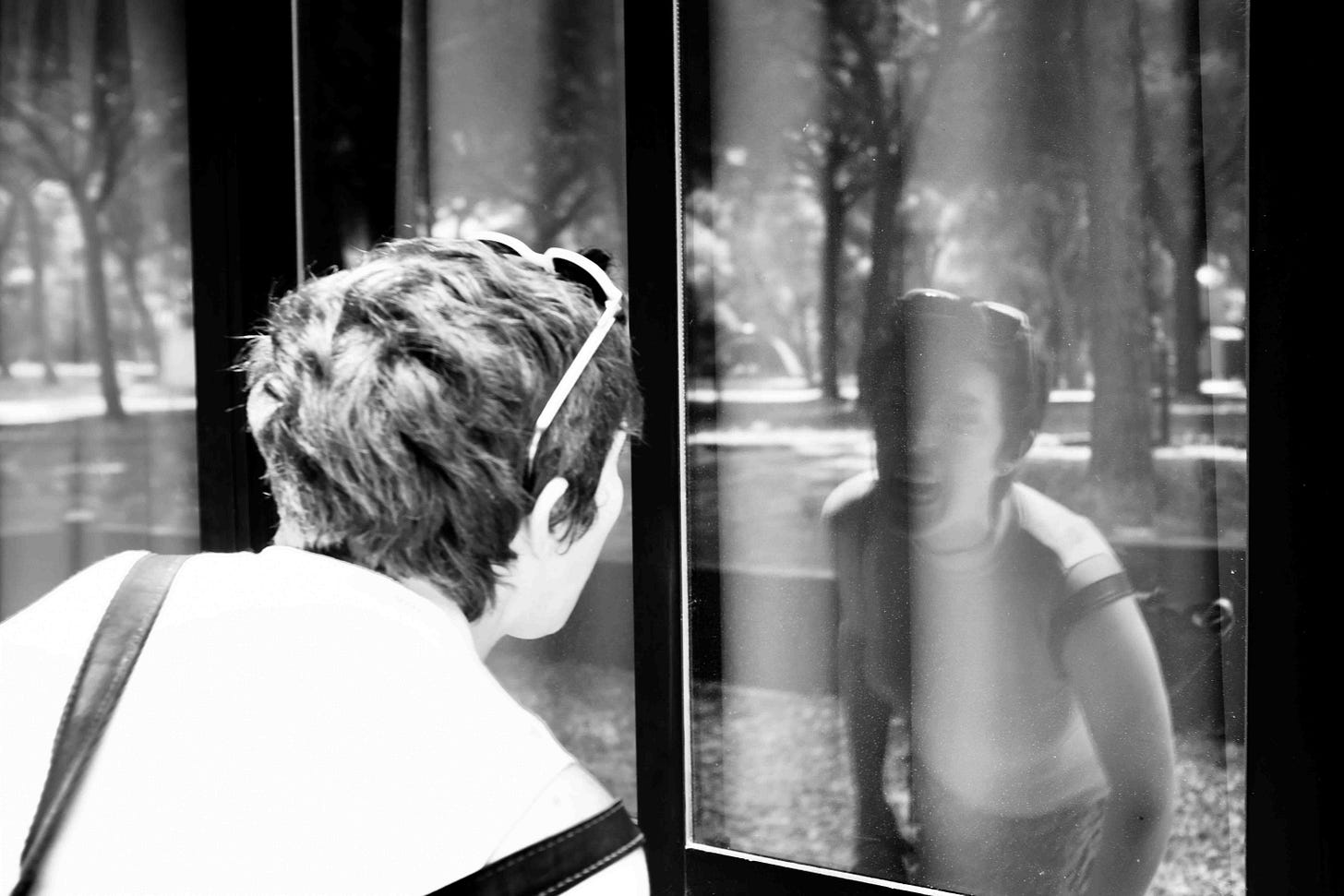 A black and white digital photo of a short-haired light-haired slim woman in her thirties looking in the reflection of a window. She is baring her teeth at herself and roaring as if she were a lion. A black and white digital photo of a short-haired light-haired slim woman in her thirties looking in the reflection of a window. She is baring her teeth at herself and roaring as if she were a lion.
