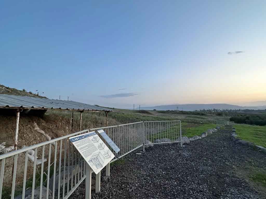 Archaeological profile at left with cover visible, walkway with sign showing information about site