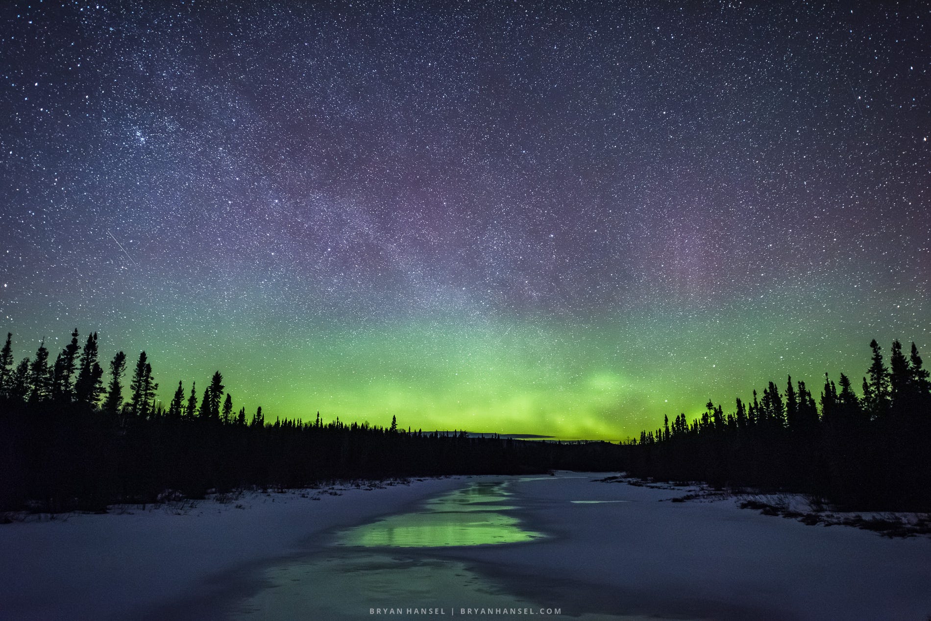 A river that has exposed ice on it reflecting the northern lights and stars above