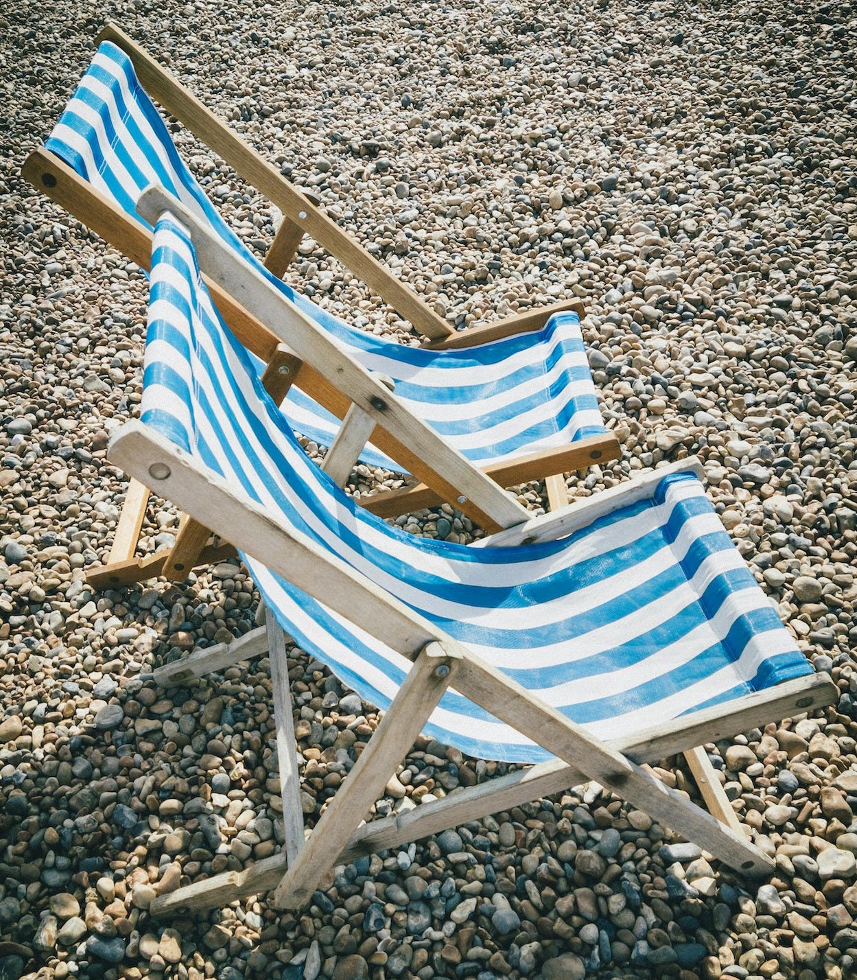 Two blue and white deck chairs on a pebbly beach Two blue and white deck chairs on a pebbly beach