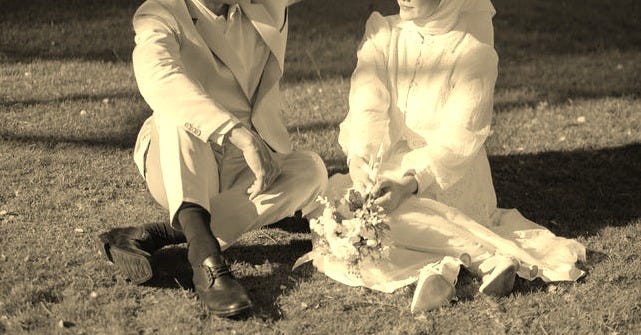 This may contain: a man kneeling down next to a woman in a white dress