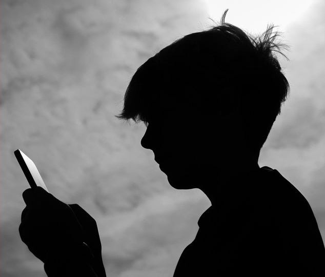 A black-and-white photograph shows a teenage boy looking at a smartphone.