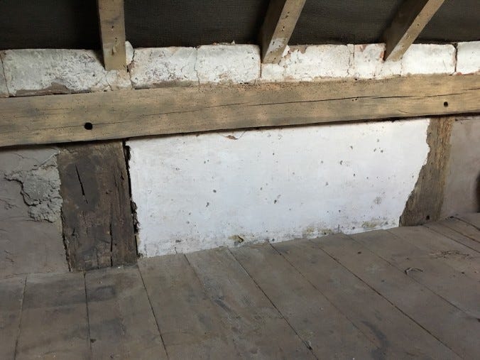 A dwarf wall with old oak beams and a row of white-washed bricks placed loosely in the gap where a soffit should be