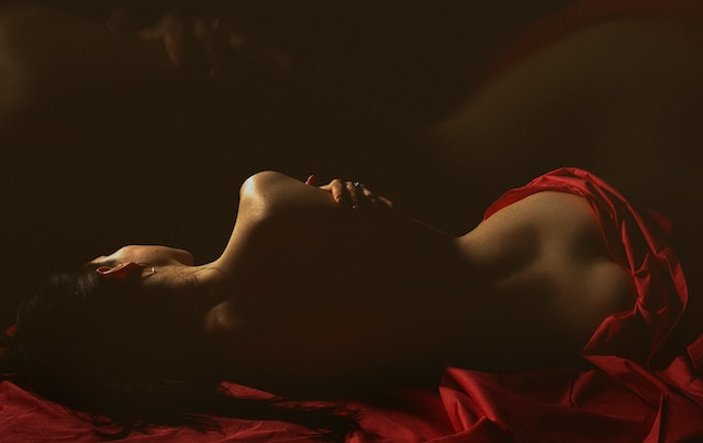 Naked woman lying on a bed with a red silk cloth draped over her, evoking a sense of passion and intimacy.