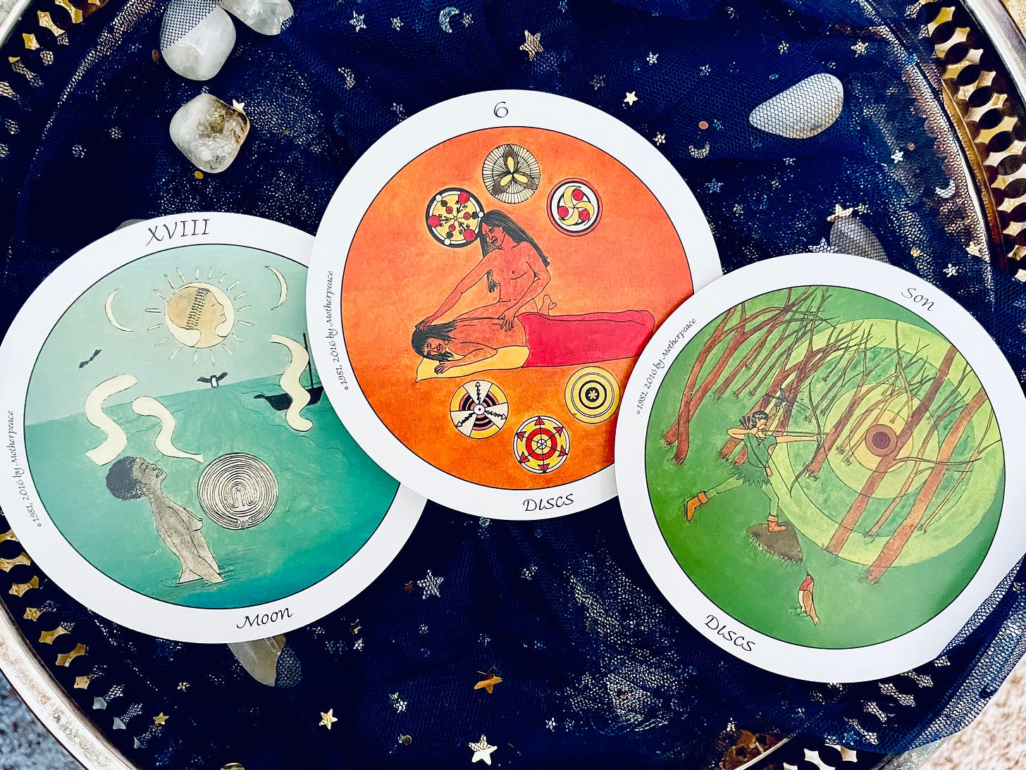 Three cards from the Motherpeace Tarot on a blue starry cloth, Moon, 6 of Discs, Son of Discs