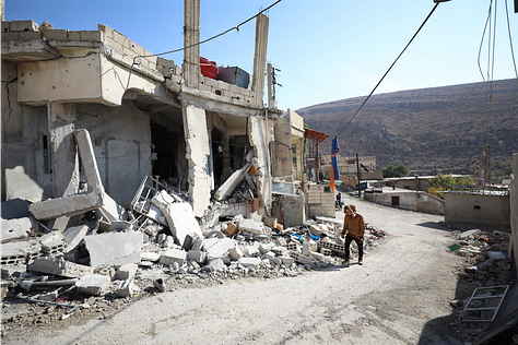 Beit Jinn in the immediate aftermath of the strike — homes torn open, streets covered in debris, and White Helmet rescuers searching for survivors beneath collapsed structures.