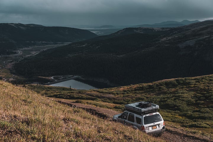 A gallery collage of eight photos from a cross-country road trip. The images show a dark-colored Ford Escape in various scenic American landscapes, including mountains, open plains at sunset, and on the road. The gallery also includes details from the journey and a view from inside the car.