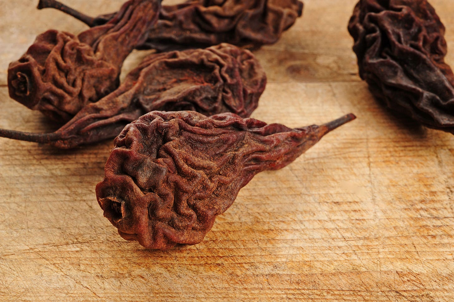 Several heavily shriveled, dark-brown dried pears with stems lie on a light wooden board; their wrinkled surface shows the typical texture of dried fruit.