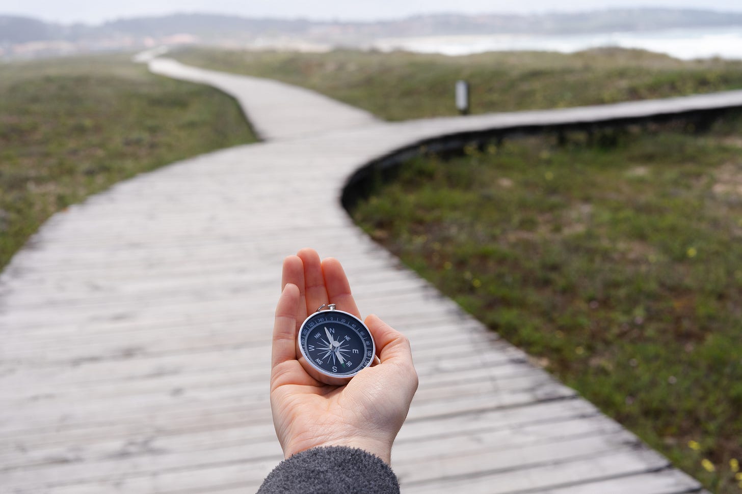 Hand holding compass in front of two diverging paths
