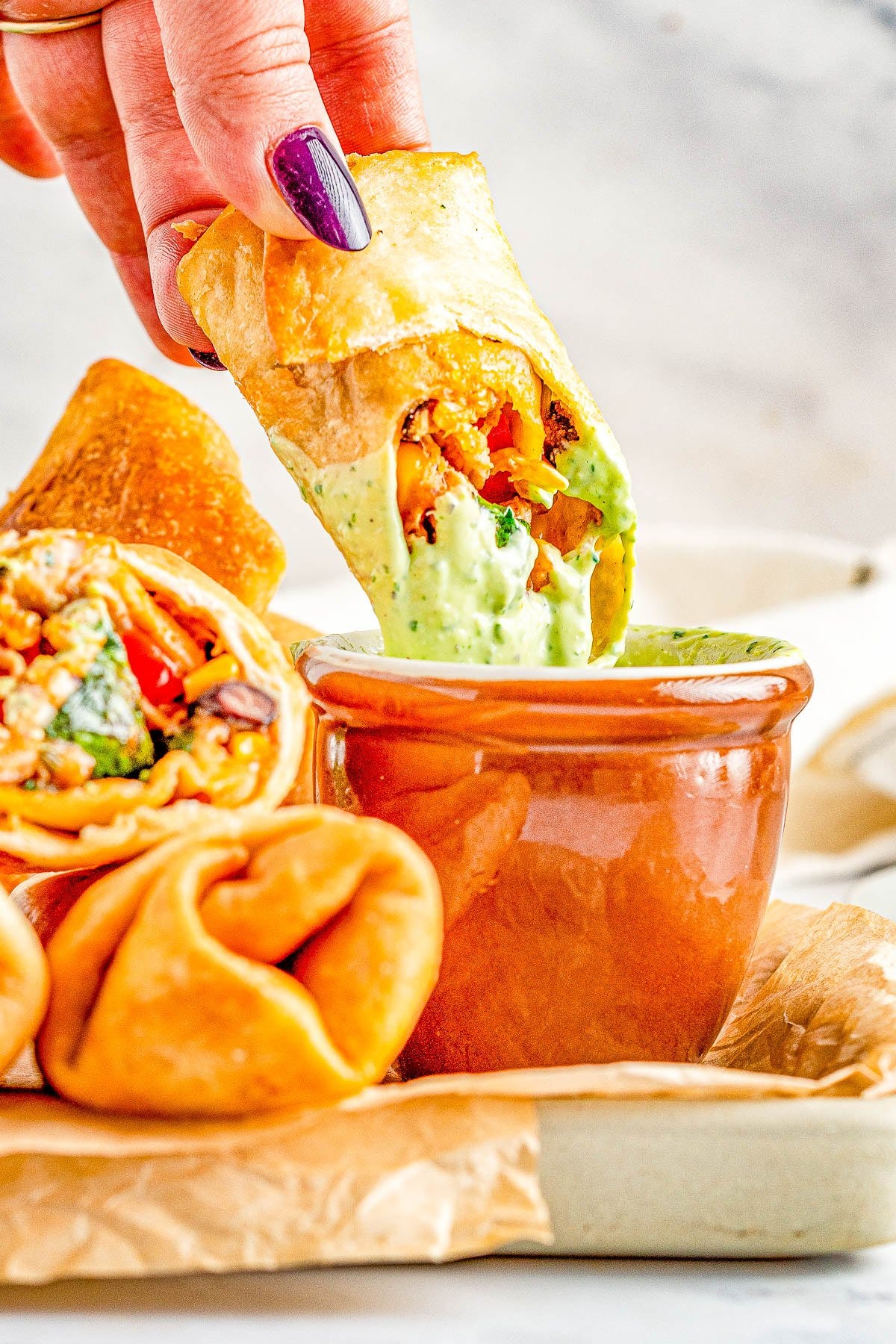 Southwestern Egg Rolls - Juicy chicken, melted Pepper Jack cheese, black beans, bell peppers, and corn seasoned with southwest-inspired seasonings and fried to crispy PERFECTION! You can fry, air fry, or bake these EASY egg rolls which are a Chili's Restaurant copycat. The quick creamy mashed avocado ranch dipping sauce is the perfect final touch! 