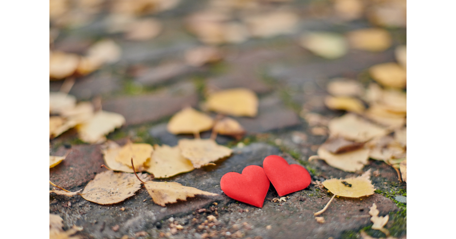 Two red heart decorations resting among autumn leaves, symbolizing love and romance.