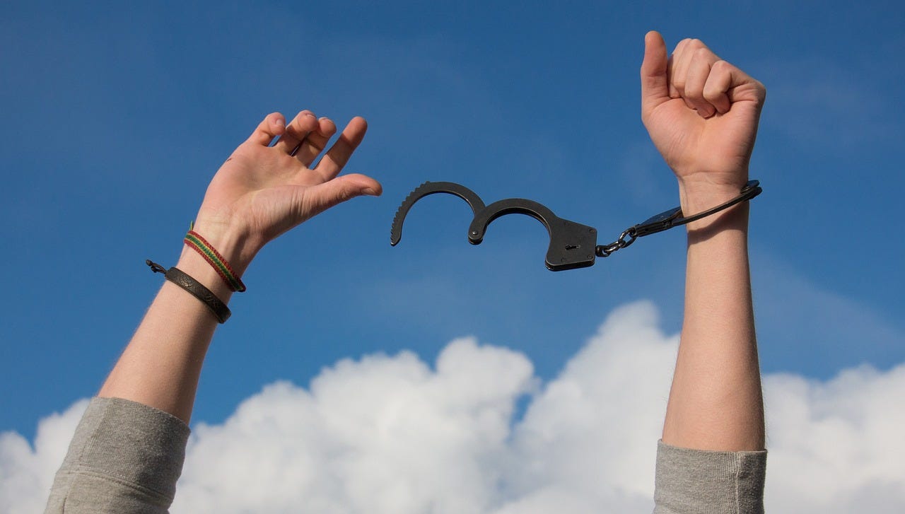 A person breaking free from handcuffs under a bright blue sky with scattered white clouds, symbolizing freedom, independence, and liberation.