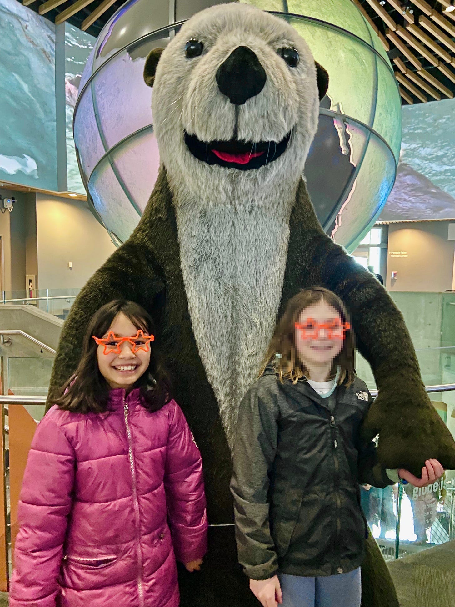 Two girls in front of giant stuffed otter.