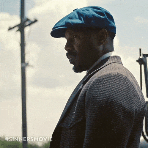 a man wearing a blue hat and a suit has #sinnersmovie written in the corner a man wearing a blue hat and a suit has #sinnersmovie written in the corner