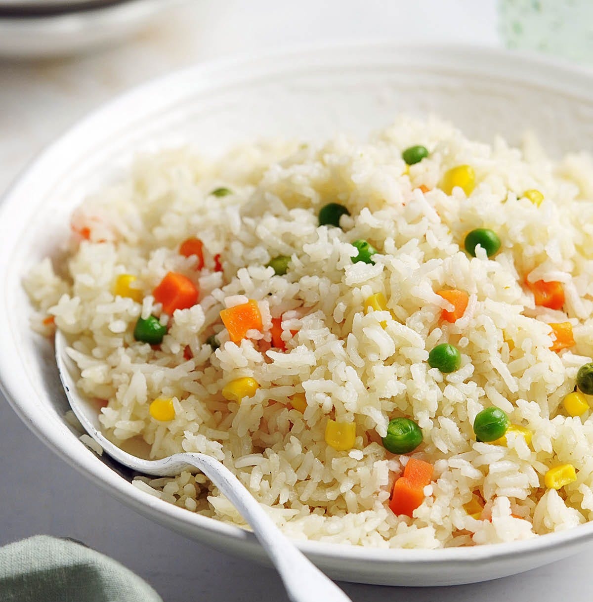 A white bowl with Arroz Primavera with a white spoon in it.