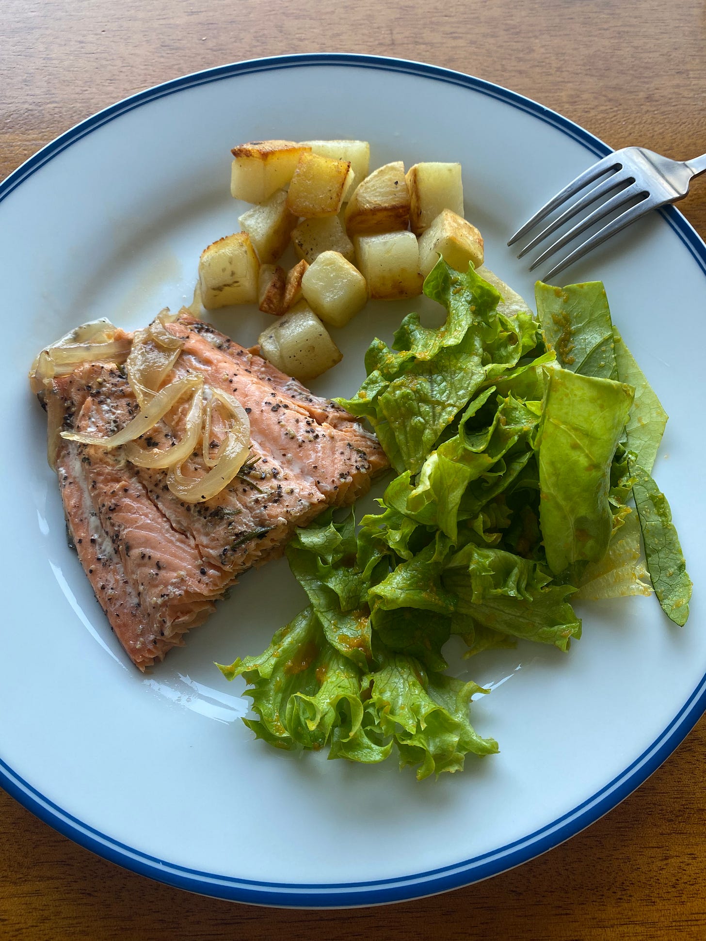 A plate with pink fish seasoned with maple soy glaze, pepper, and caramelized onions, next to cubes of roasted potato and a green salad. 