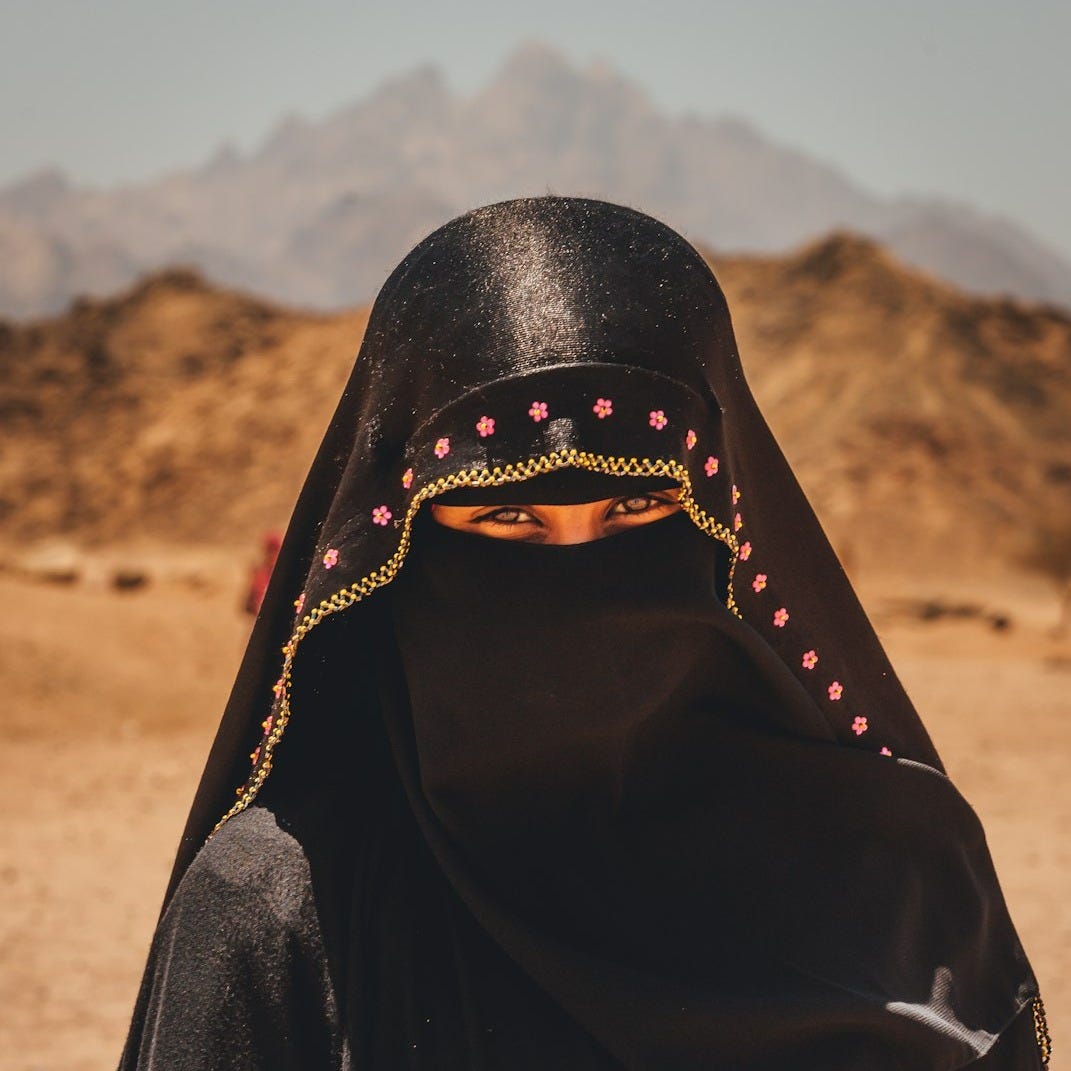 person in black hijab standing on brown field during daytime