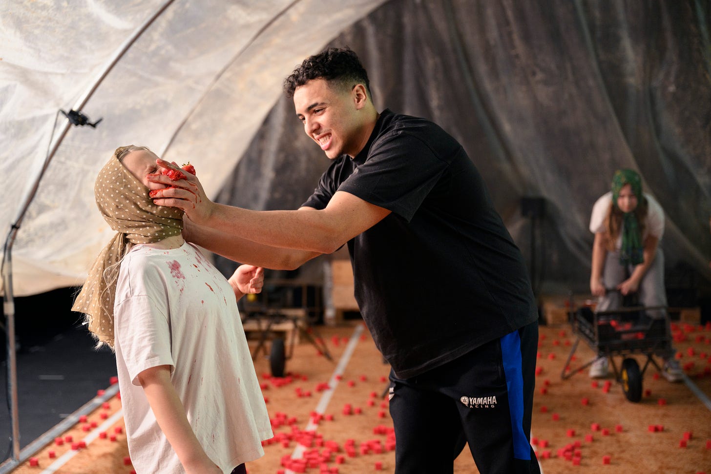 A young girl wearing a headscarf has a strawberry mashed in her face by man.