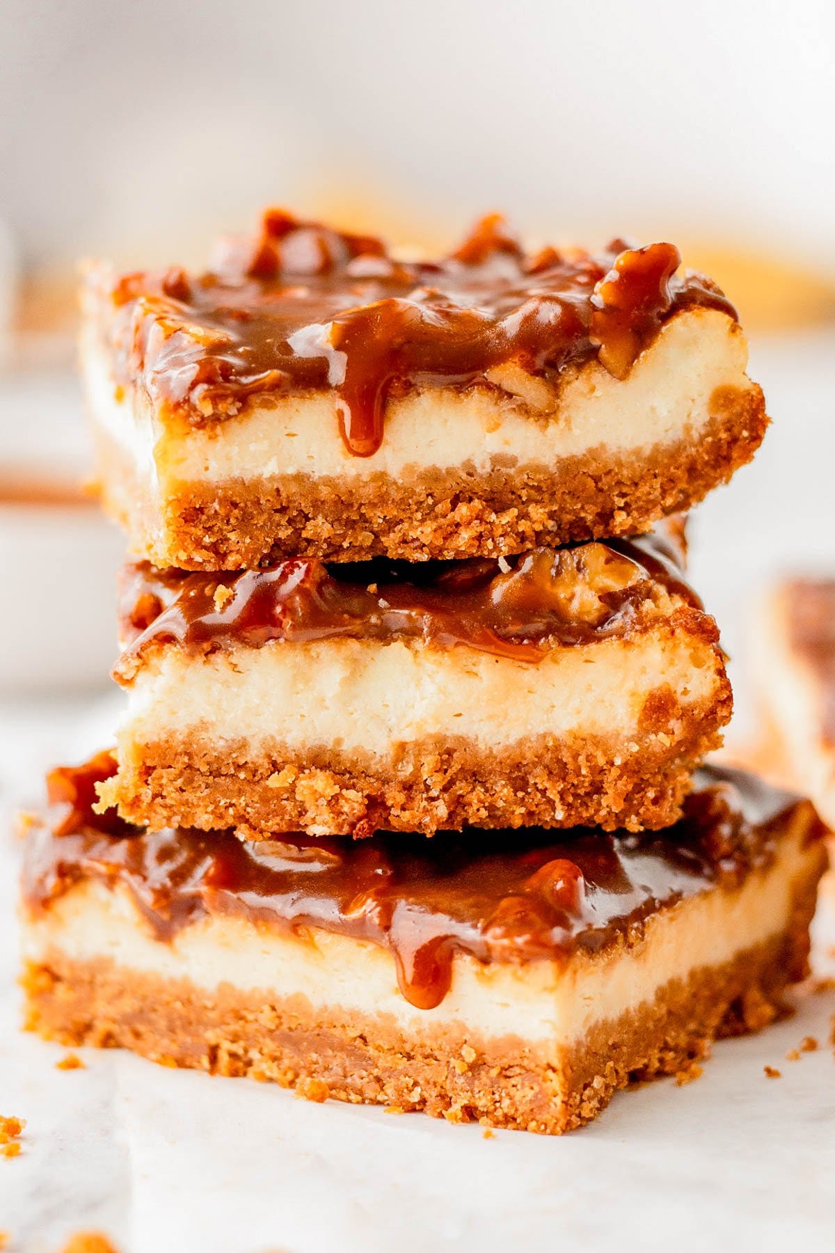 Three caramel cheesecake bars with a graham cracker crust are stacked on top of each other, with caramel sauce dripping down the sides. Three caramel cheesecake bars with a graham cracker crust are stacked on top of each other, with caramel sauce dripping down the sides.