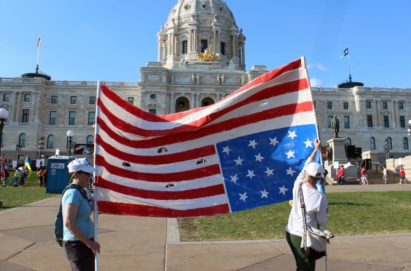 two people marching in front of the state capitol building are holding an upside down american flag two people marching in front of the state capitol building are holding an upside down american flag