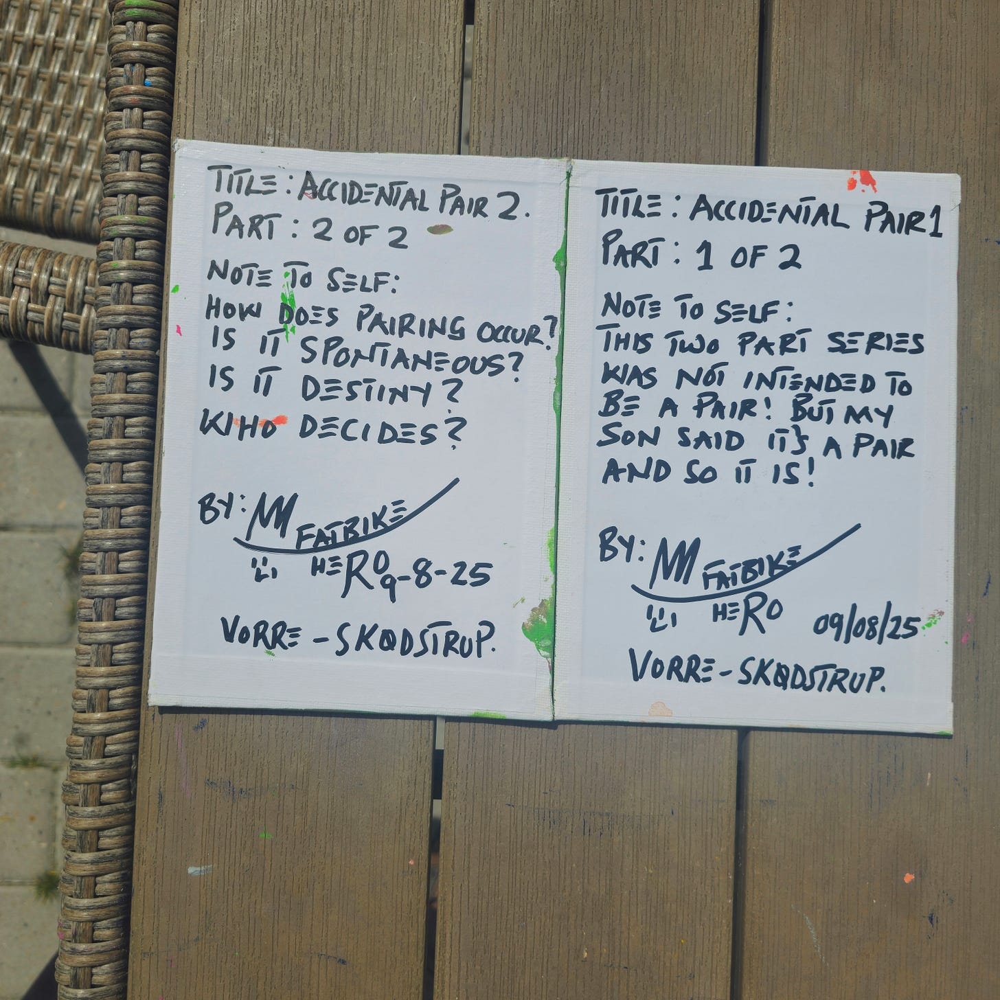 The back of two canvas panels showing handwritten notes in black marker. The right panel reads: "Title: Accidental Pair 1... Note to self: This two part series was not intended to be a pair! But my son said it's a pair and so it is!" The left panel poses questions about destiny and spontaneity. Signed by M Fatbike Hero, Vorre-Skødstrup.