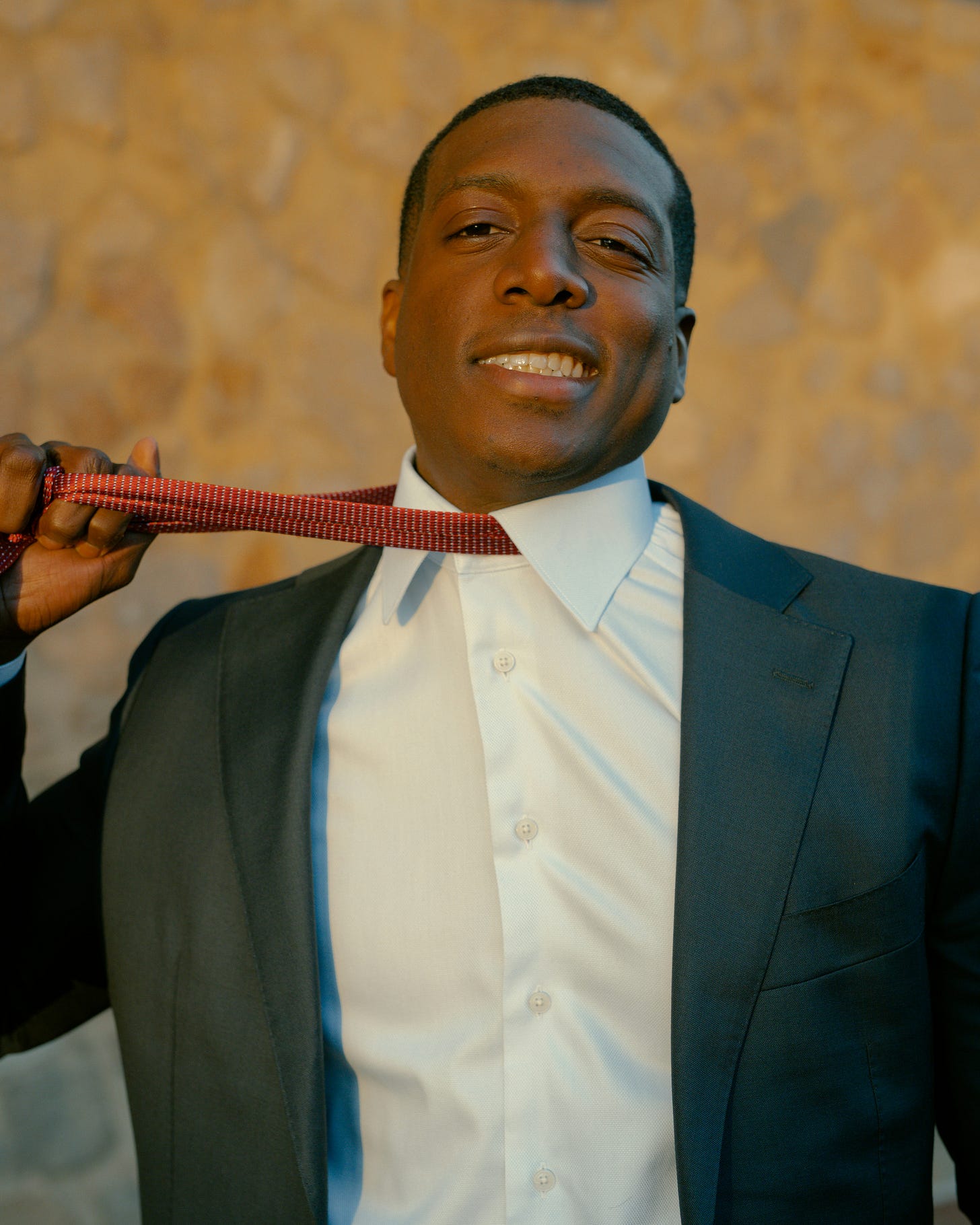 Professional Black man in dark suit adjusting red patterned tie, smiling confidently - representing midlife career change and Legacy Pivot transformation