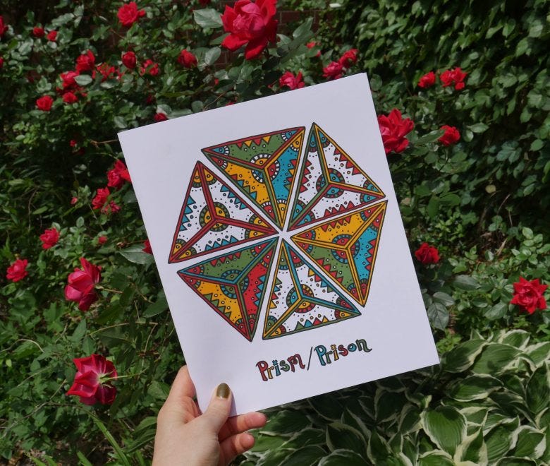 A white hand holds a copy of Prism/Prison up in front of a large red rose bush. The magazine is white with black lettering for the title and features a color illustration of a six-sided geometric shape filled in with red, yellow, blue, and green abstract patterns.
