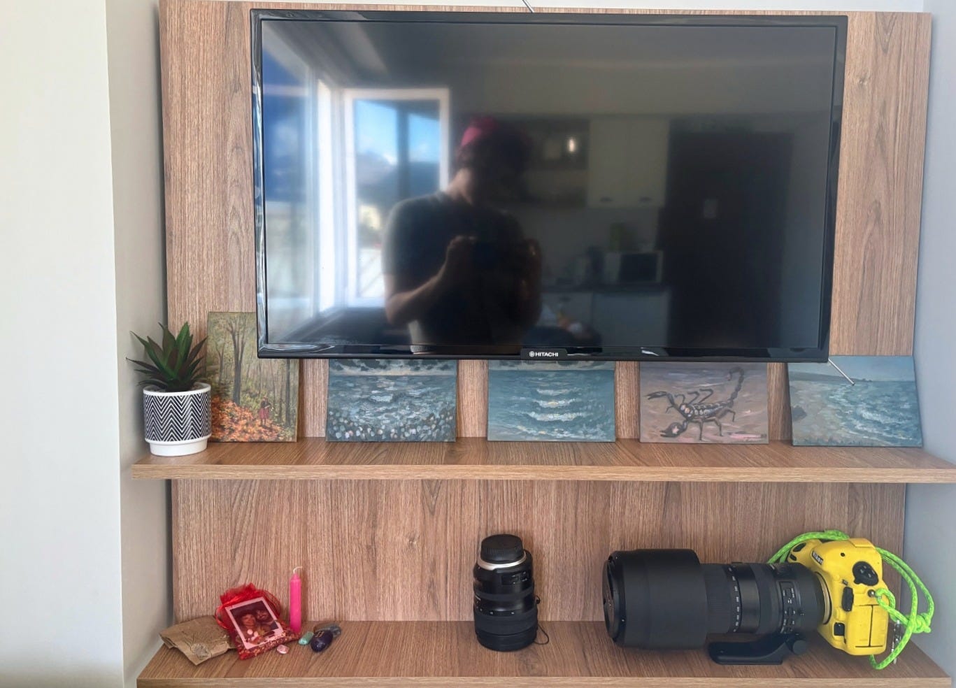 five small panels on shelf under tv reflecting person taking photograph, another shelf below holding small ritual items and camera with large lens