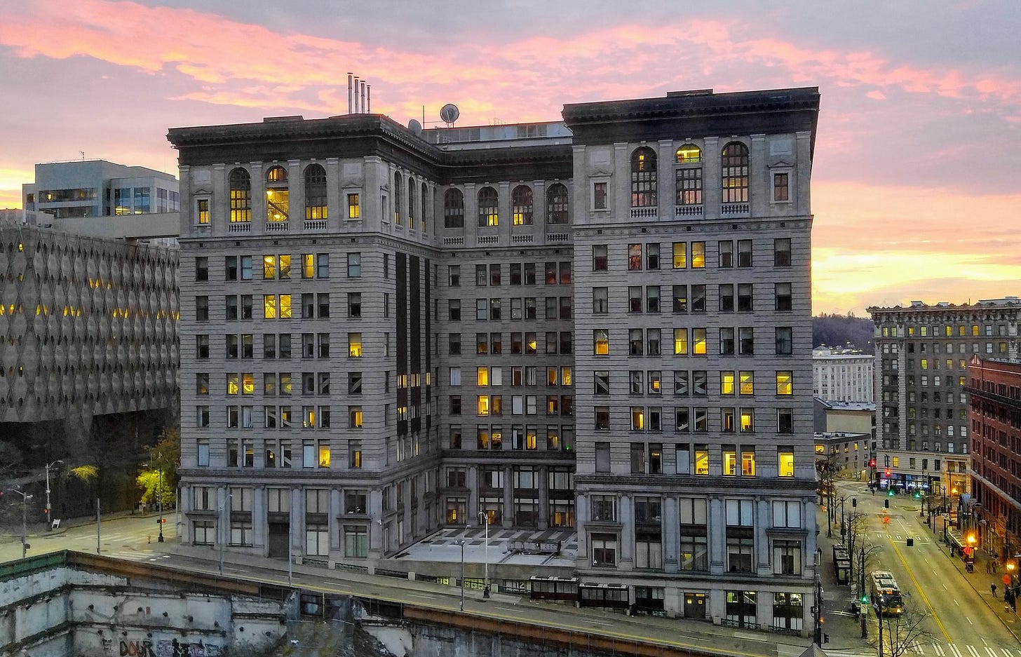 King County Courthouse in Seattle photographed at dawn, its stone facade lit warmly against a pink and orange sky. Street lights and traffic signals glow along the intersection below.