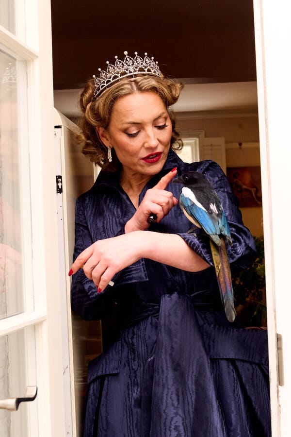 Sitwell, in a tiara, taps the beak of her pet magpie, who sits on her arm.