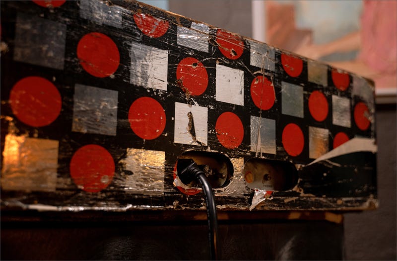 The back of a Wurlitzer 140b that is wrapped with a pattern of silver foil squares and red circles. There is an IEC power cable plugged into the amplifier.