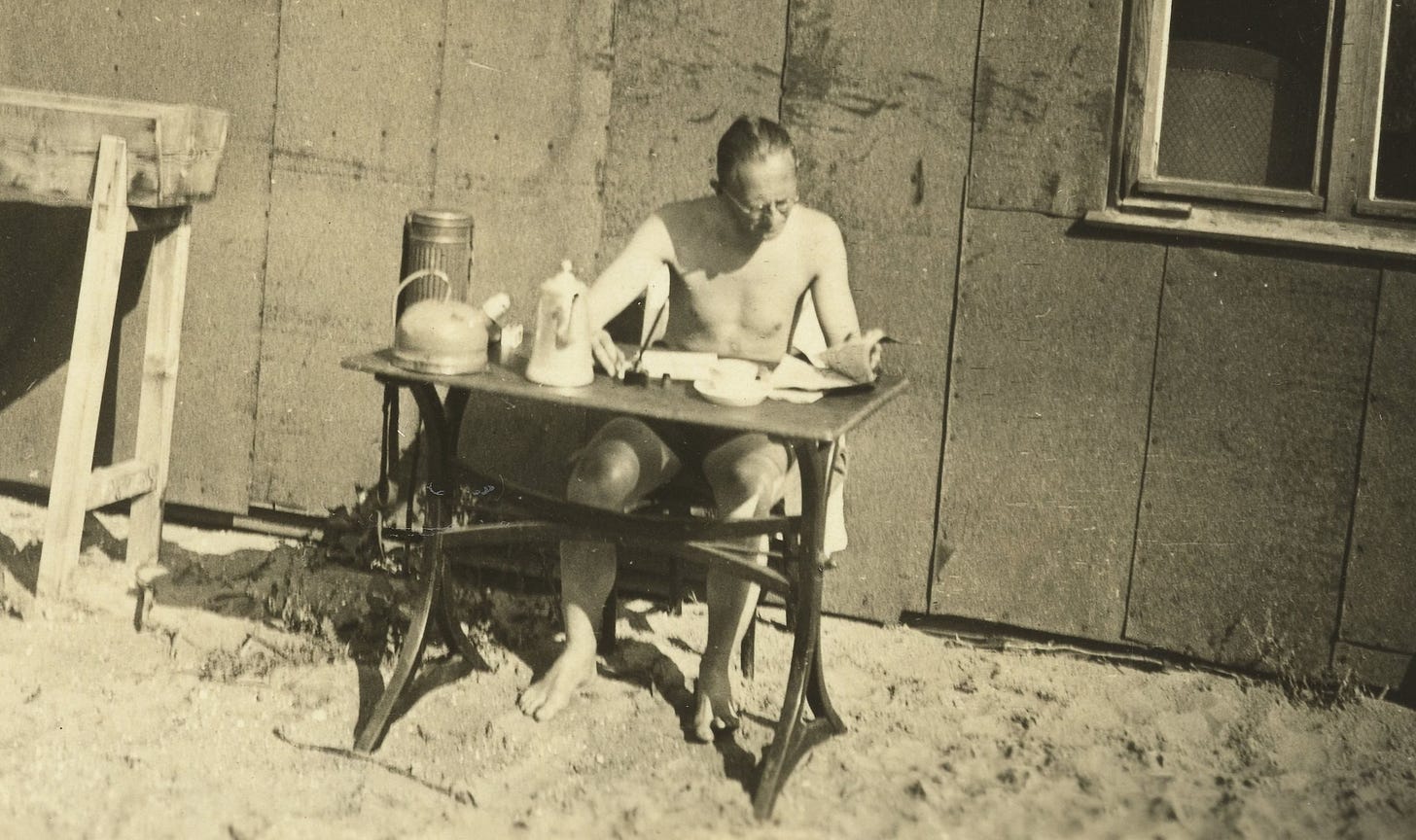 Man reading a magazine at a table on a beach.