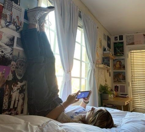 This may contain: a person laying on a bed with a book in their hand and looking at the screen