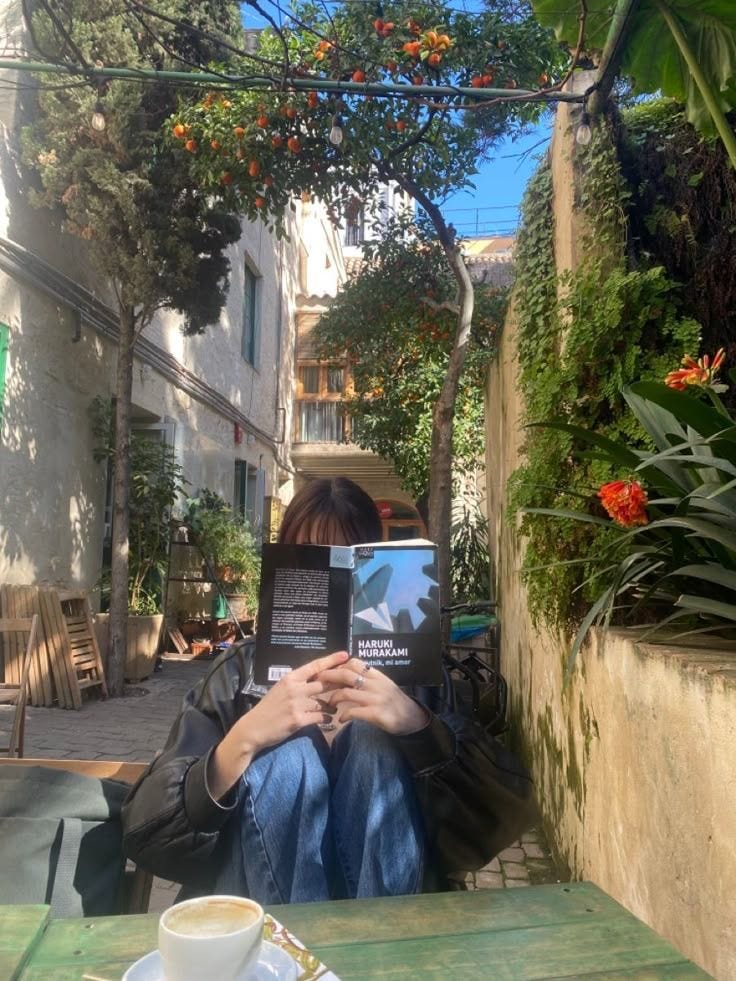 This may contain: a person sitting at a table with a book on their lap and coffee in front of them This may contain: a person sitting at a table with a book on their lap and coffee in front of them