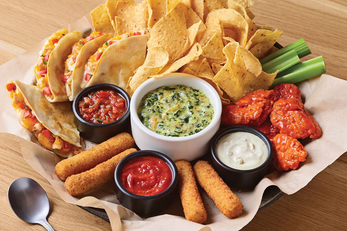 An Applebee's appetizer sampler including tortilla chips, buffalo wings, mozzarella sticks, quesadillas, and spinach dip.