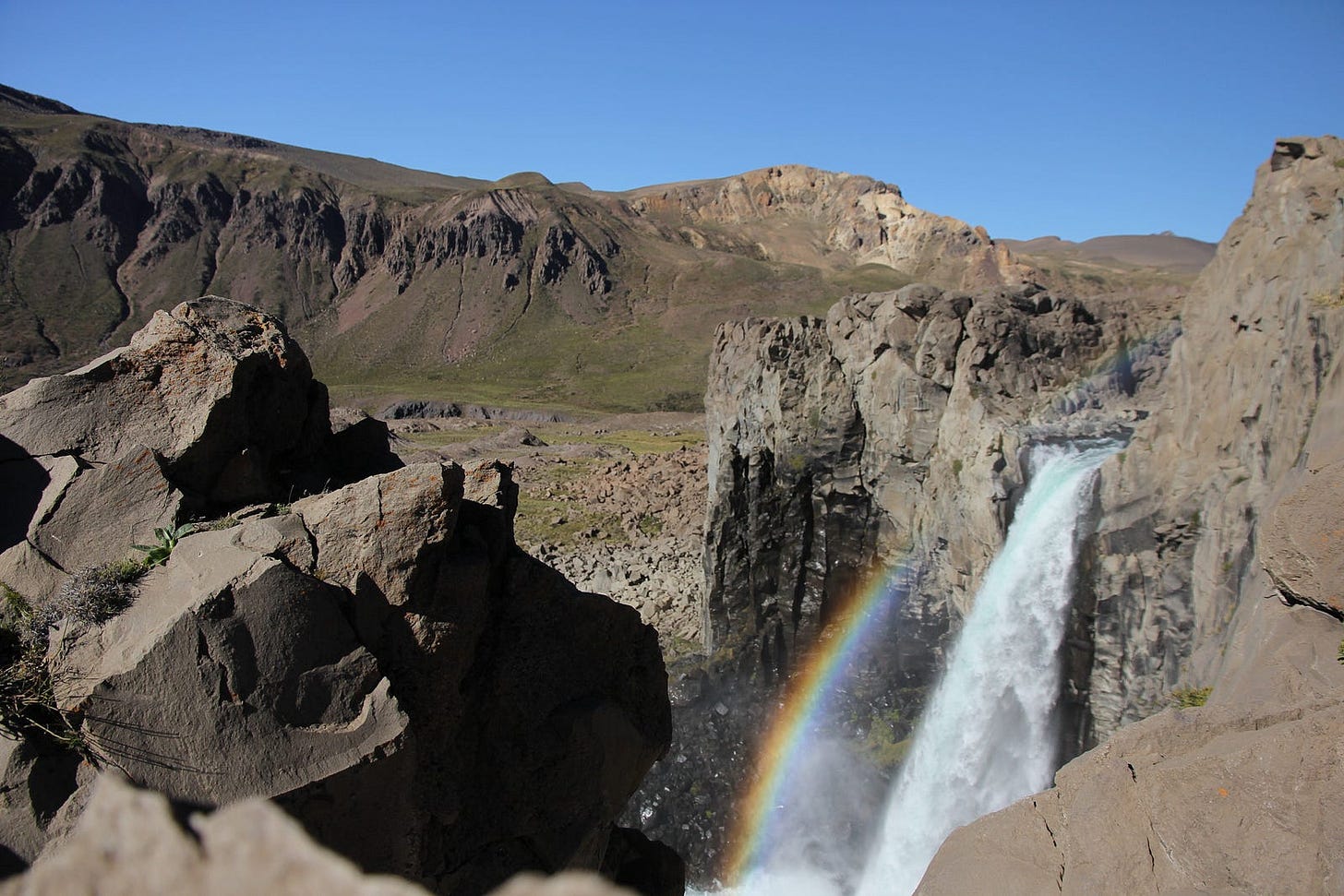 Waterfall in arid terrain with a rainbow above the falling water