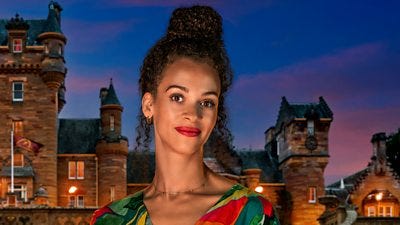A woman in a multicoloured top smiles to camera wearing bold red lipstick, set against the background of a castle by night A woman in a multicoloured top smiles to camera wearing bold red lipstick, set against the background of a castle by night