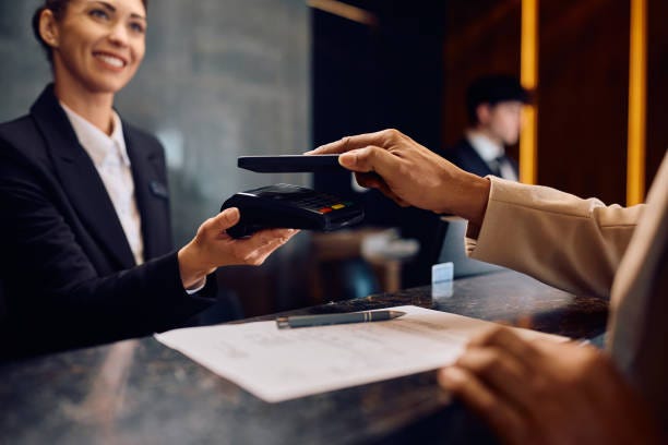 Close up of black man using smart phone while paying in a hotel. Close up of hotel guest paying contactless with his mobile phone at reception desk. Payment Management in hotel  stock pictures, royalty-free photos & images