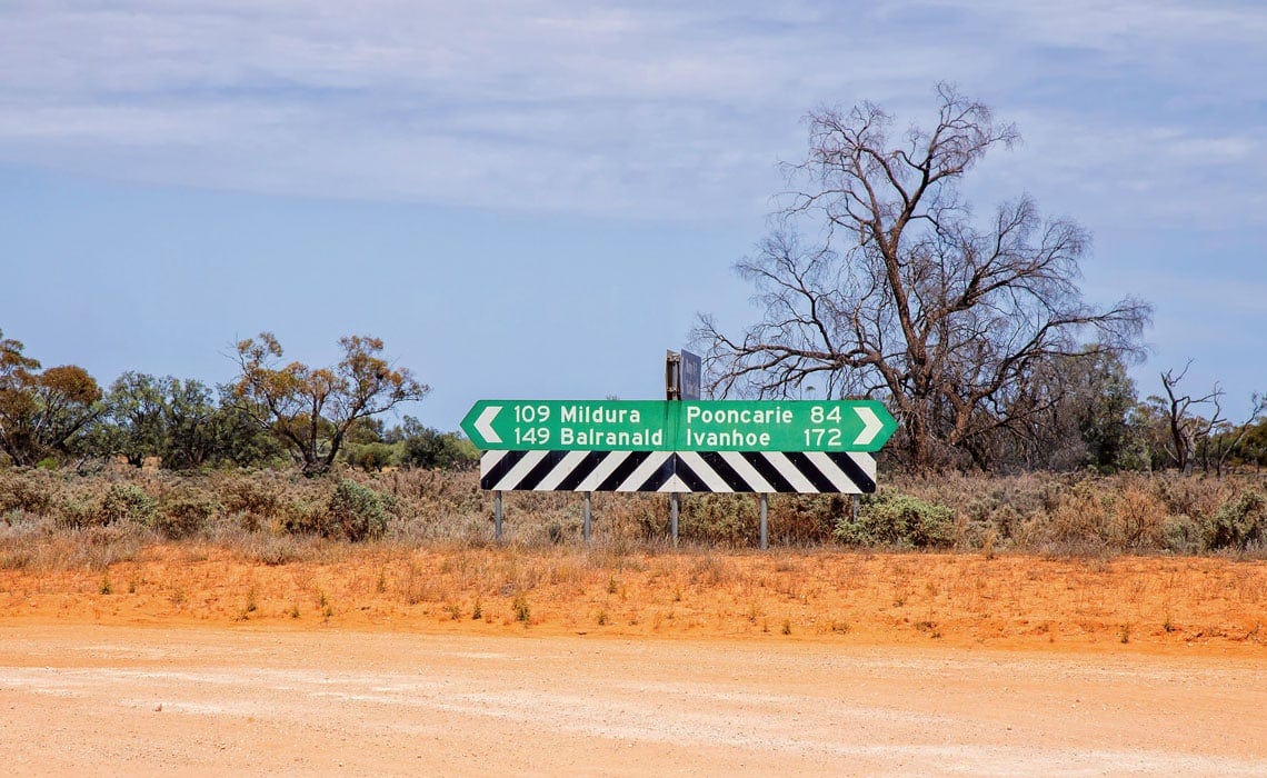 Dirt road with roadsign indicating Pooncarie to the east and Mildura to the west
