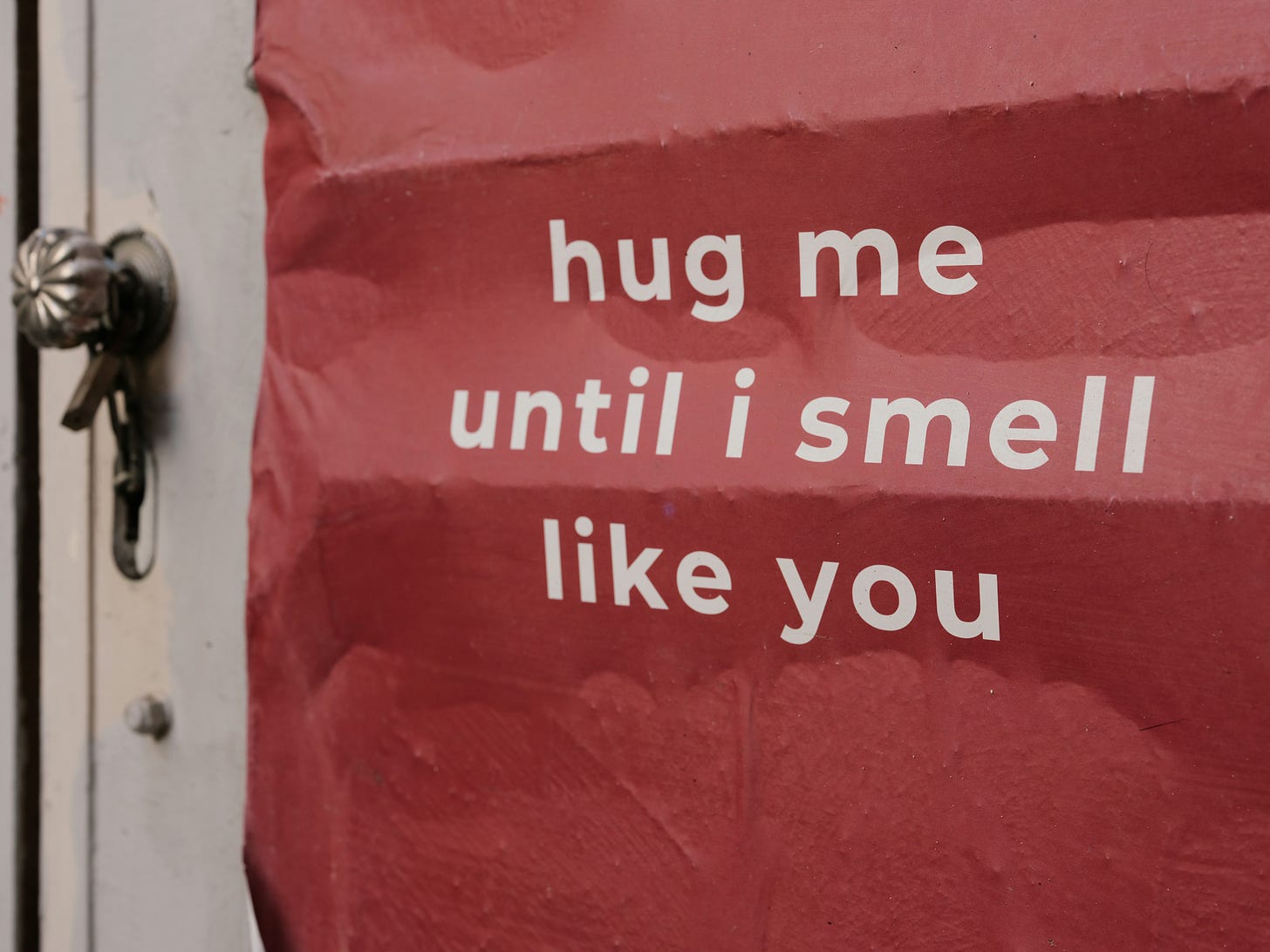 white door, silver knob, red construction paper on the door with white letters, "hug me until I smell like you"