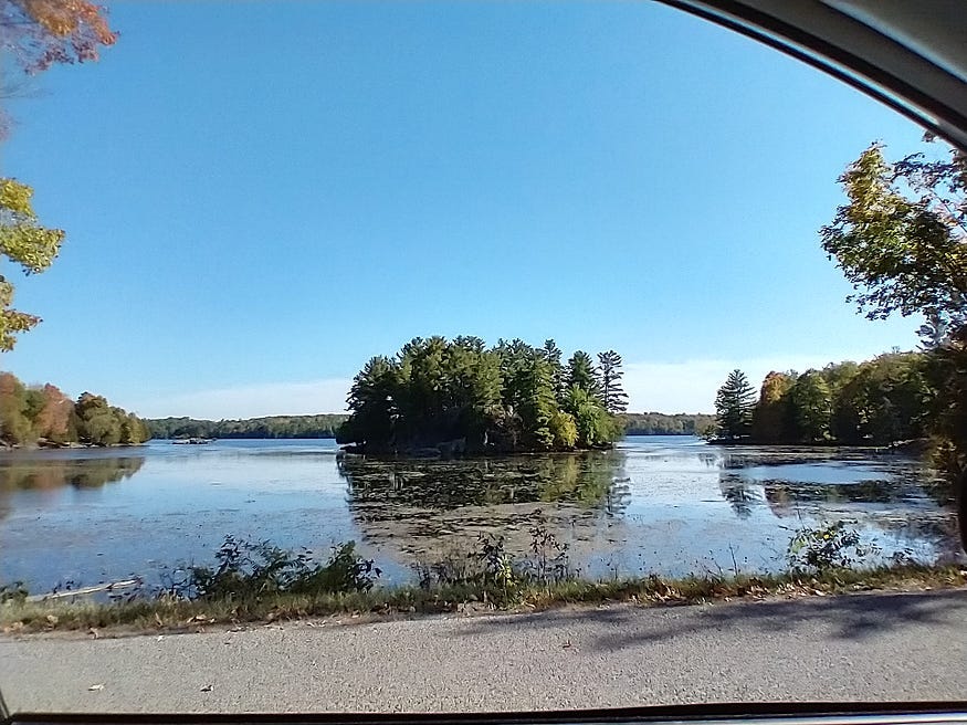 A small island just offshore in Lake Opinicon, as seen from Opinicon Road. Blue skies and fall colours.