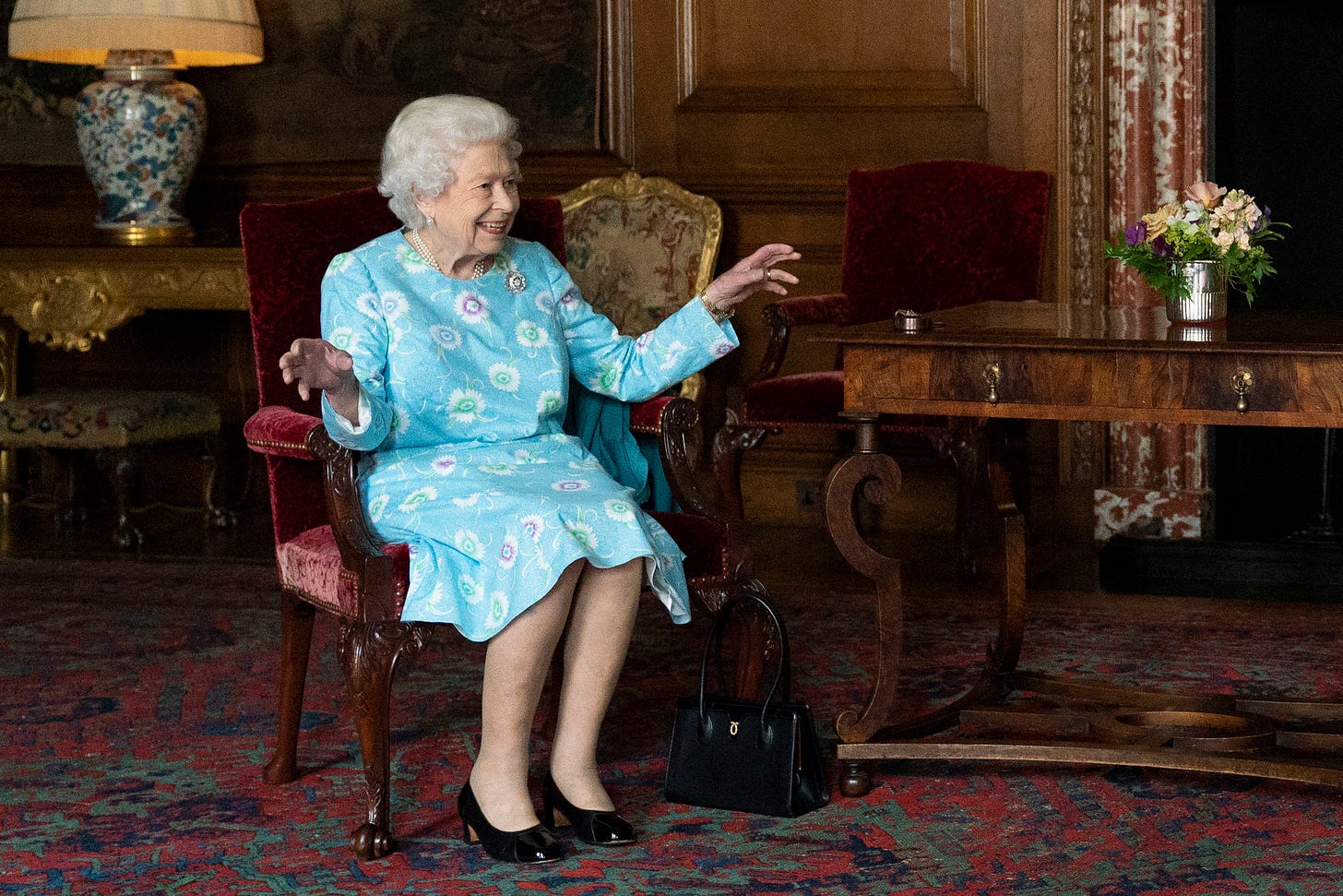 Queen Elizabeth II sitting in a chair in a blue dress