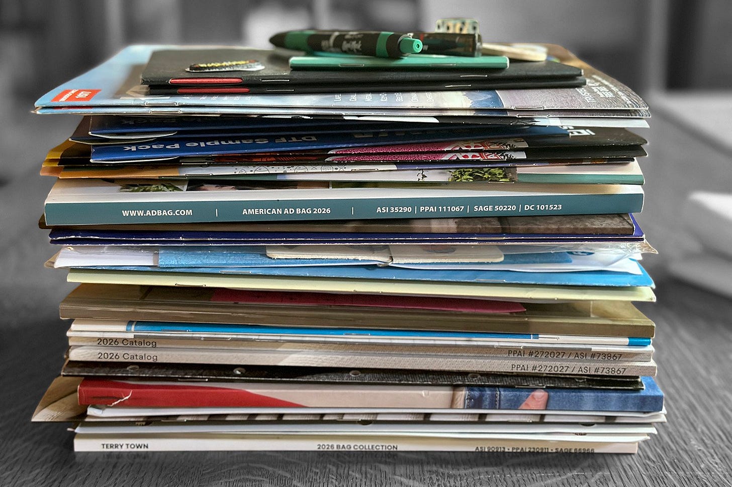 Stack of promotional product catalogs, notebooks, and pens collected at the 2026 ASI Show.
