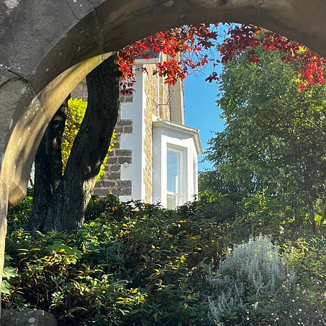 glimpse of a garden beyond a stone archway, the view beneath a low bridge, a grand stone house behind black iron railings