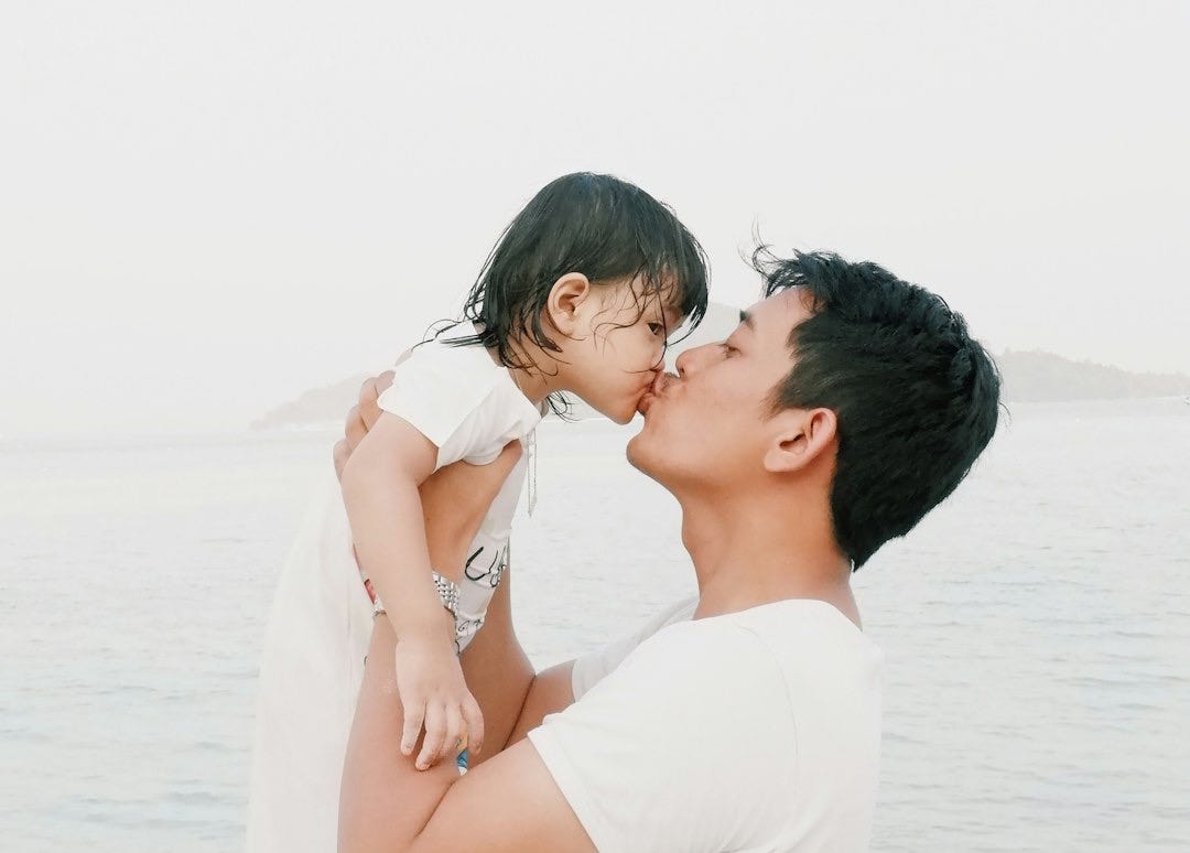 man kissing toddler during daytime
