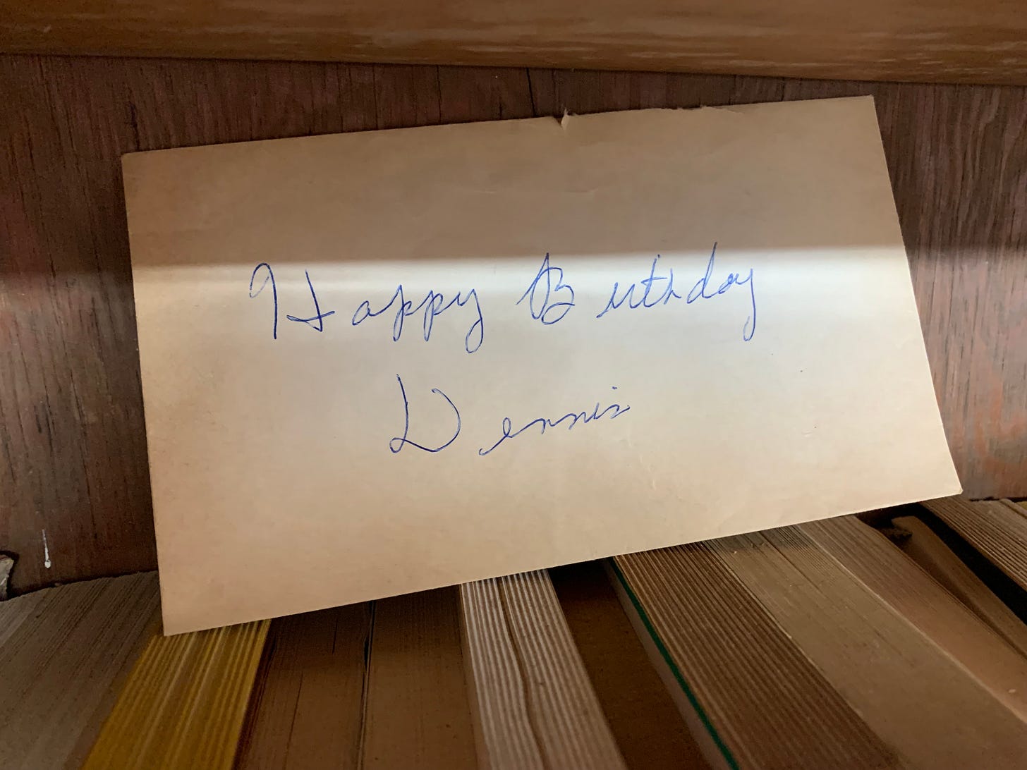 An old yellowed envelope resting atop a row of books that reads, "Happy Birthday Dennis"